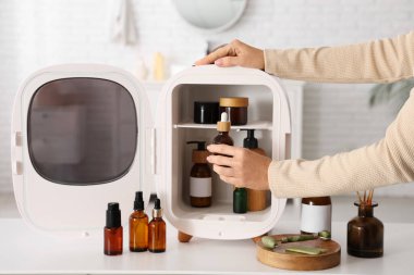 Kadın eller, beyaz arka plandaki küçük kozmetik buzdolabından gerekli yağı alıyor. Yakın çekim.