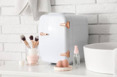 Küçük kozmetik buzdolabı, makyaj fırçaları ve sünger odadaki beyaz tuğla duvarın yanındaki masada. Yakın çekim.