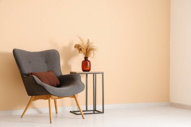 Siyah koltuk ve kahve masası. Odadaki bej duvarın yanındaki vazoda otlar var.