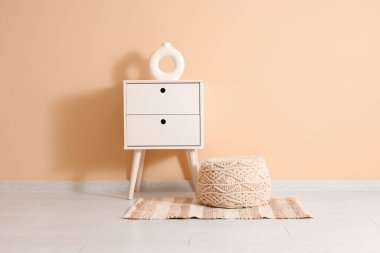 Komodinin yanında ve odada bej duvarın yanında puf.