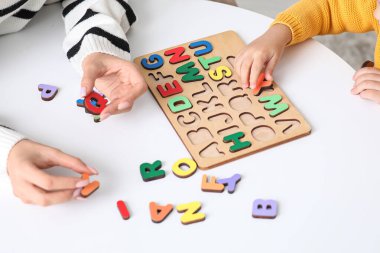 Öğretmen ve harf tahtası olan küçük kız masada alfabeyi öğreniyor, yakın plan.