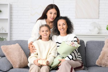 Genç Asyalı bir kadın, evdeki kanepede annesiyle kız kardeşine sarılıyor.