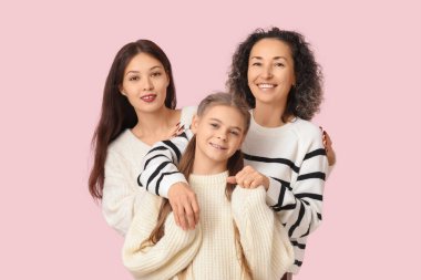 Kızları pembe arka planda kucaklaşan olgun bir kadın.