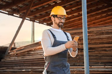 Erkek marangoz kereste fabrikasında cep telefonu kullanıyor.