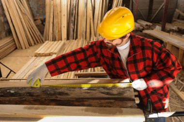 Erkek marangoz kereste fabrikasında ahşap kalas ölçüyor.