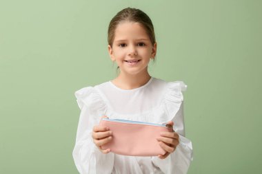 Yeşil arka planda kalem kutusu olan şirin, mutlu bir kız.