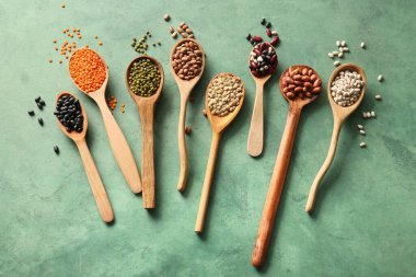 Yeşil arka planda farklı baklagillerin ahşap kaşıklarıyla kompozisyon