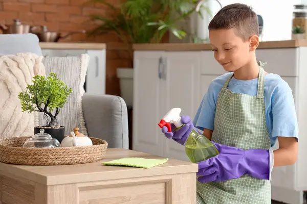 Paçavra ve spreyle evde kahve masasını temizleyen sevimli bir çocuk.