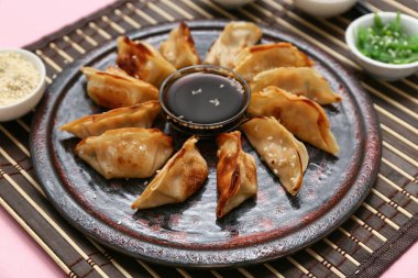 Kızarmış Japon gyoza tabağı ve pembe arka planda soya sosu, yakın plan.