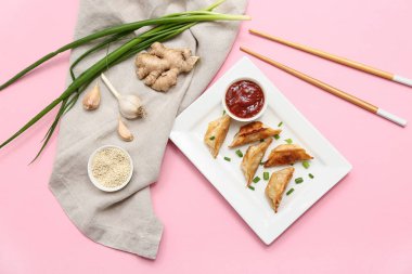 Pembe arka planda yeşil soğanlı ve bir kase soslu kızarmış Japon gyozası.