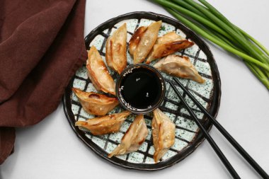 Bir tabak kızarmış Japon gyoza ile bir kase soya sosu ve gri arka planda yeşil soğan.