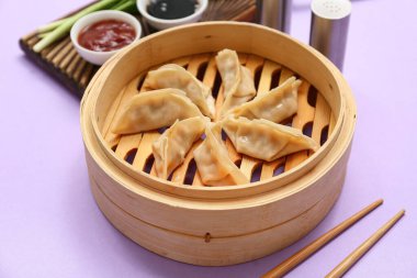 Lezzetli Japon gyoza 'lı bambu buharı ve leylak arka planda bir kase sos.