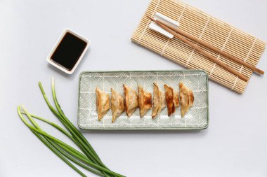 Bir tabak kızarmış Japon gyoza ile bir kase soya sosu ve gri arka planda yeşil soğan.