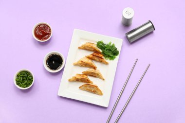 Bir tabak kızarmış Japon gyozası, deniz yosunu salatası ve leylak arkaplanlı soslar.