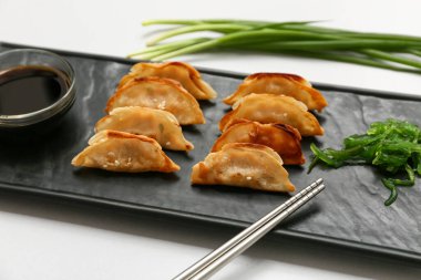 Kızarmış Japon gyozası, deniz yosunu salatası ve gri arka planda bir kase soya sosu.