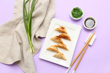 Bir tabak soya soslu kızarmış Japon gyozası ve leylak arkaplanlı yosun salatası.