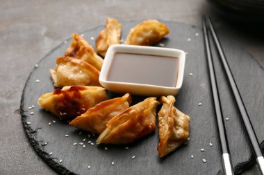 Kızarmış Japon gyozası ve siyah arka planda bir kase soya sosu.