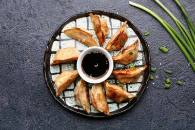 Koyu arkaplanda yeşil soğanlı ve bir kase soya soslu kızarmış Japon gyozası.