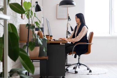 Modern ofiste bilgisayarla çalışan genç bir kadın.