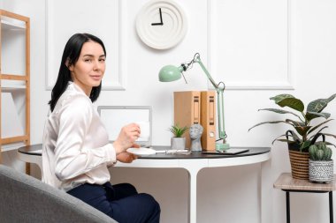 Ofiste bir fincan kahveli genç bir kadın oturuyor.