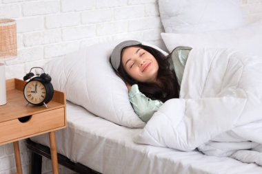 Çalar saati olan genç bir kadın yatak odasında yatıyor.