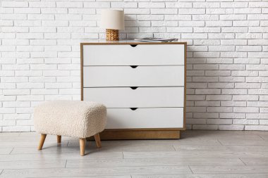 Oda beyaz tuğla duvarın yanında lambalı çekmeceler.