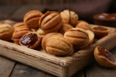 Ahşap arka planda kaynamış yoğunlaştırılmış sütle ceviz şekilli kurabiyeler kesme tahtası, yakın plan.