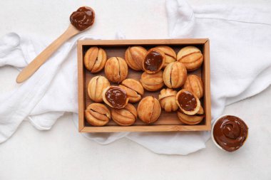 Ahşap kutu, beyaz arka planda kaynamış konsantre süt ve ceviz şeklinde kurabiyeler.