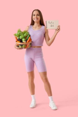 Elinde KETO diyeti ve pembe arka planda yemek olan genç bir kadın.