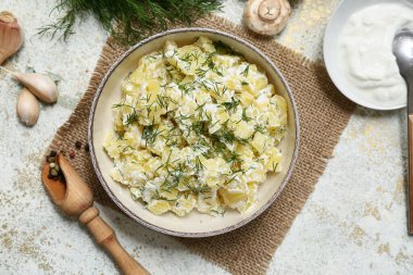 Bir kase lezzetli patates salatası, dereotlu, mantarlı, ekşi kremalı ve beyaz grunge arka planda biberli.