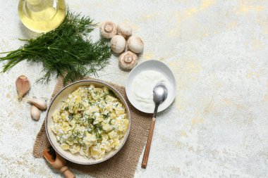 Bir kase lezzetli patates salatası, dereotu, mantar, ekşi krema ve beyaz grunge arka planda bir sürahi yağ.