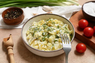 Bir kase lezzetli patates salatası, dereotlu, domatesli, biberli ve bej rengi grunge arka planda sarımsaklı.