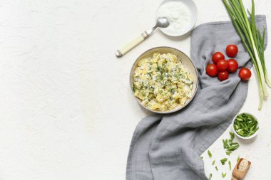 Bir kase lezzetli patates salatası, yeşil soğan, domates, ekşi krema ve beyaz arka planda susam tohumu.