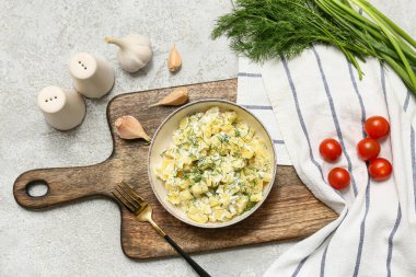 Bir kase lezzetli patates salatası, dereotlu, yeşil soğanlı, domatesli ve grunge arkaplanda sarımsaklı.