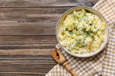 Bir kase lezzetli patates salatası, dereotlu ve ahşap arka planda bir kepçe biber.