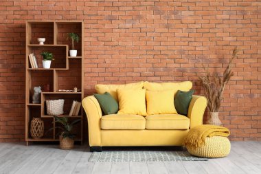 Sarı kanepe ve raf ünitesinde yastıklar olan oturma odasının içinde.