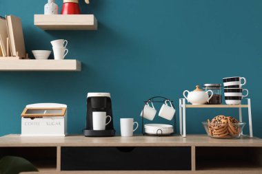 Kahve makinesi, fincanlar ve kurabiyeler mavi duvarın yanındaki odada.