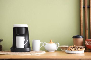 Yeşil duvarın yanındaki klozette fincanlı, şekerli ve kurabiyeli kahve makinesi.