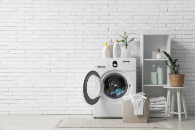 Çamaşırhane içi çamaşır makinesi, sepet ve deterjan dolu.