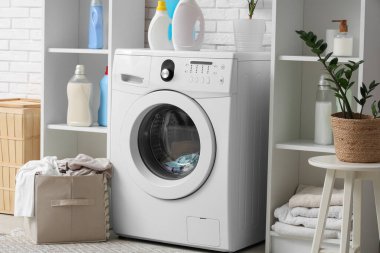 Çamaşır makinesi, deterjan şişeleri ve sepeti olan bir çamaşırhane.