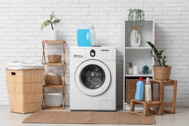 Çamaşırhane içi çamaşır makinesi, sepet ve deterjan dolu.