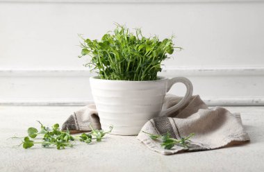 Seramik fincanda taze mikro yeşil lahanalar ve ışık masasında peçete var.