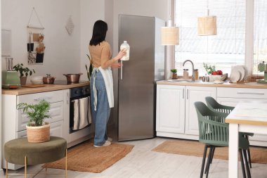 Genç bir kadın modern buzdolabını şık bir mutfakta açıyor.