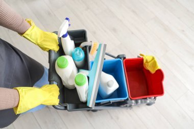 Evinin ahşap zemininde temizlik malzemeleriyle dolu tramvayı olan kadın hademe.