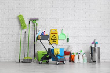 Beyaz tuğla duvarın yanında bir sürü temizlik malzemesi ve uyarı levhası olan bir araba.