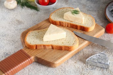 Ahşap tahta ekmek dilimleri, lezzetli işlenmiş peynir üçgenleri ve gri arka planda domatesler.