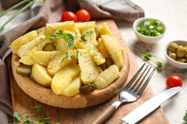 Tahta tabak lezzetli patates salatası, salatalık turşusu ve beyaz arka planda domates.