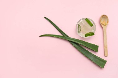 Bir kase taze aloe vera jeli, pembe arka planda yapraklar ve kaşık.