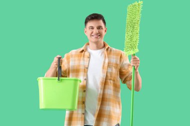 Yeşil arka planda paspas ve kova taşıyan genç bir adam.