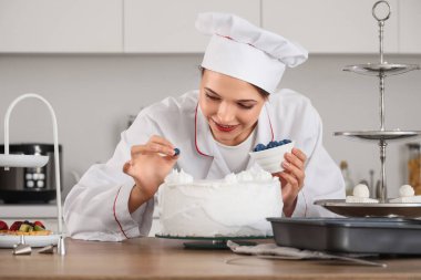 Kadın pastacı mutfakta yaban mersinli pasta yapıyor.